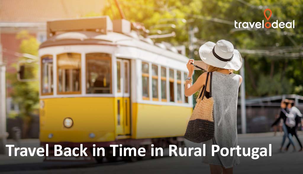 A woman in a sun hat photographs a vintage yellow tram in a charming rural Portuguese setting.