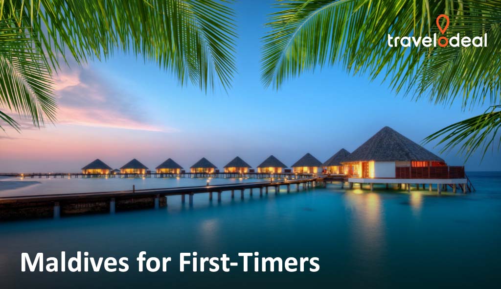 Thatched overwater villas line a wooden pier above calm turquoise sea at sunset, framed by palm leaves; “Maldives for First-Timers” text.