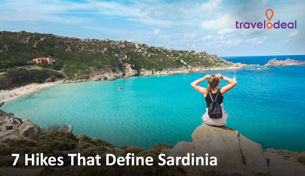 Woman sits on a rocky cliff overlooking a turquoise Sardinian bay with green hills, sandy beach, and calm sea; text overlay present.