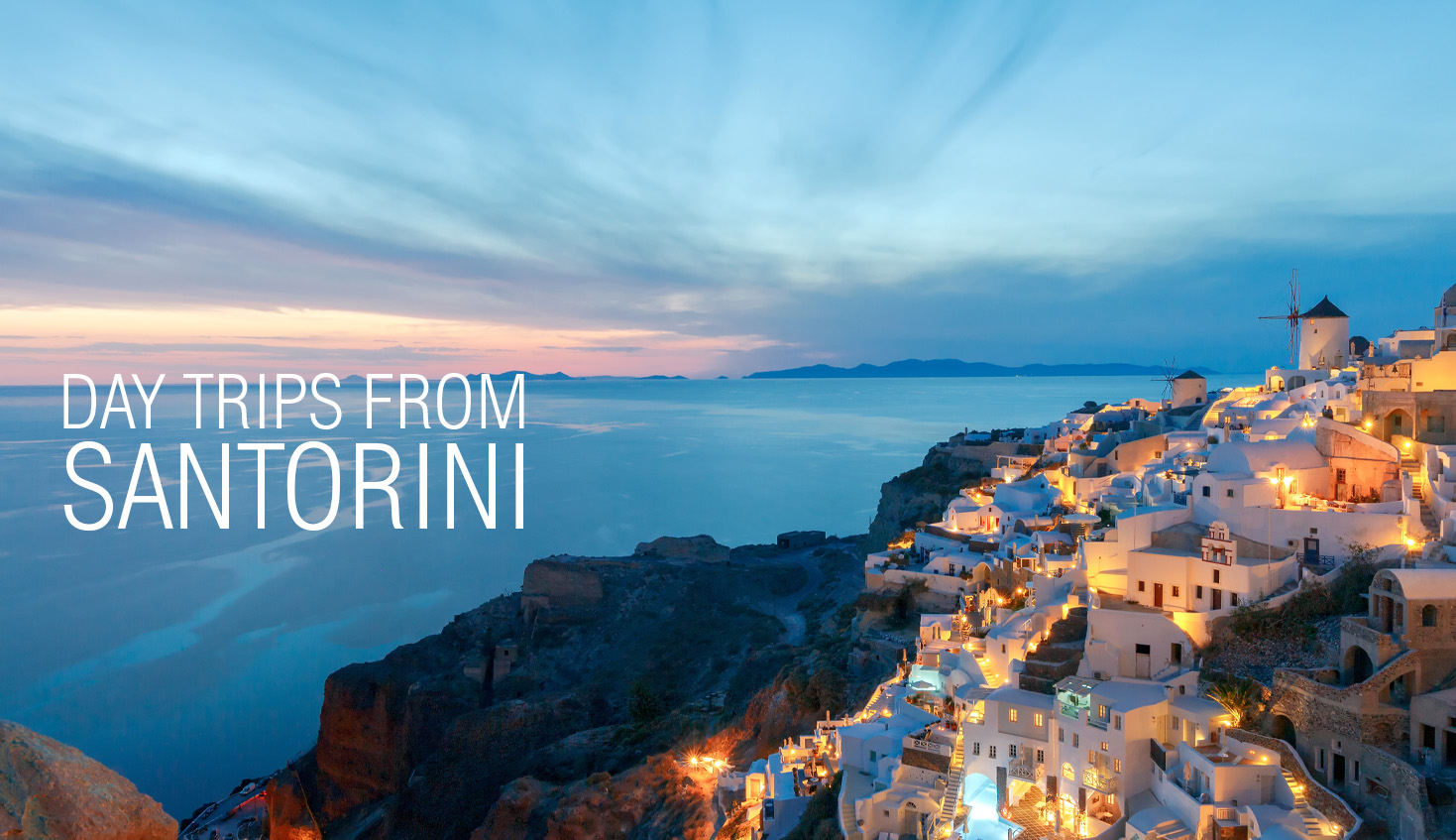View of Santorini's white buildings lit up at dusk, overlooking the sea with the sunset sky in the background.